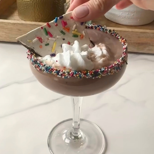 Chocolate ice cream martini in a sprinkle-rimmed coupe glass topped with whipped cream and bark