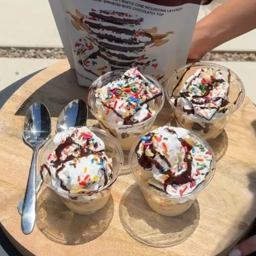Four ice cream sundae cups topped with whipped cream, sprinkles and chocolate syrup